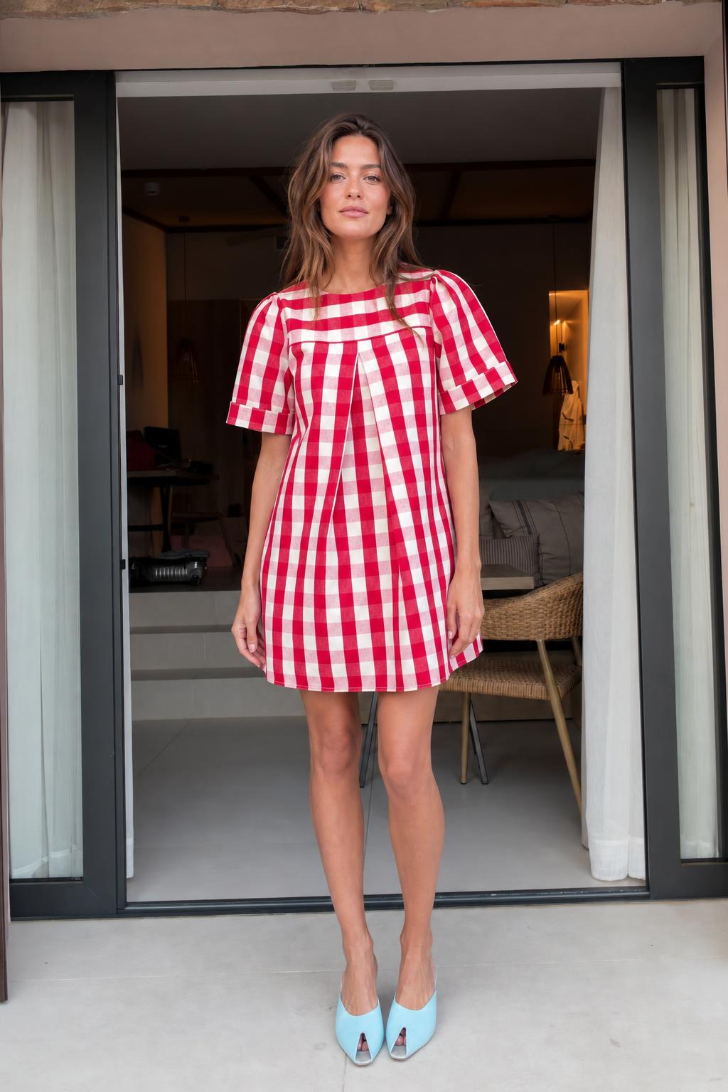Front view of woman wearing red gingham check pleated mini dress with light blue heels