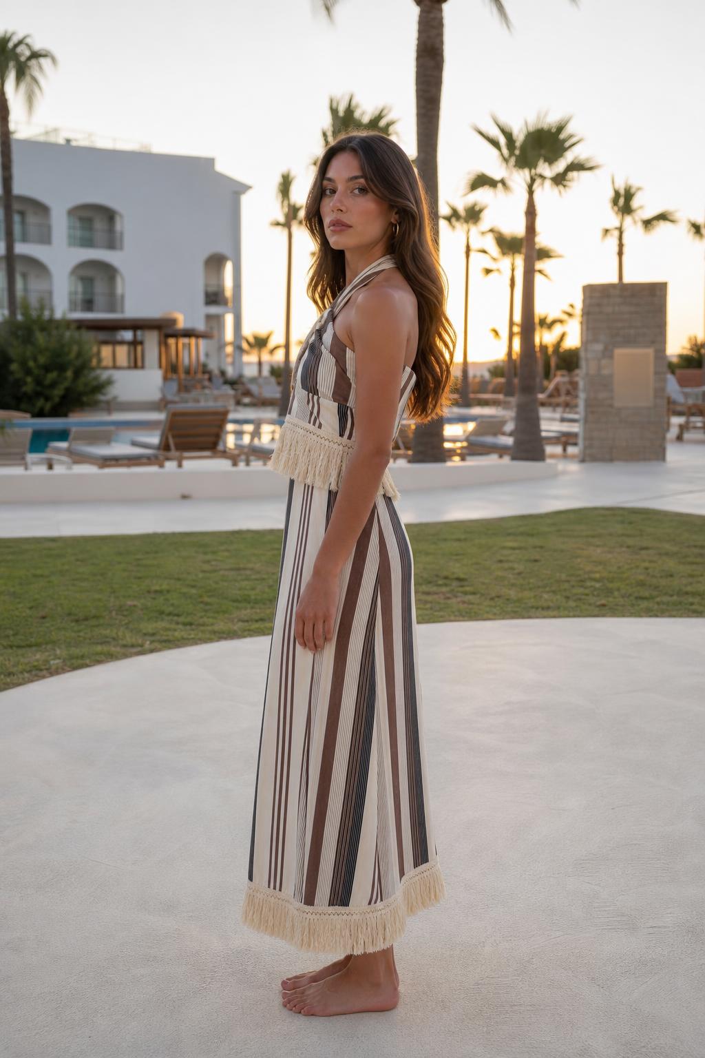 Side profile of model wearing beige stripe halter fringe maxi dress