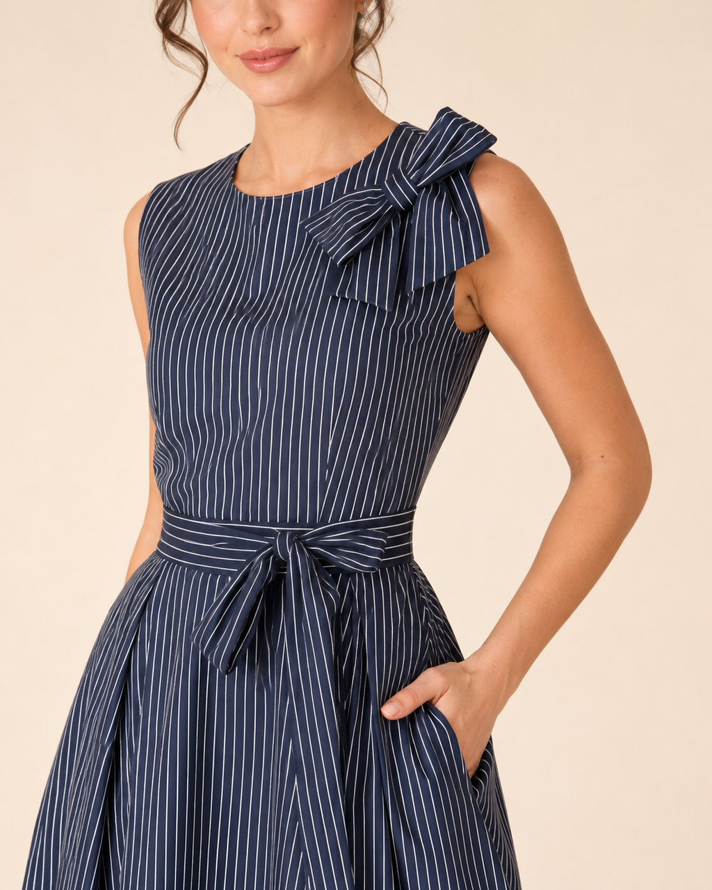 Close-up front detail of navy striped midi dress with shoulder bow, round neckline, and waist tie