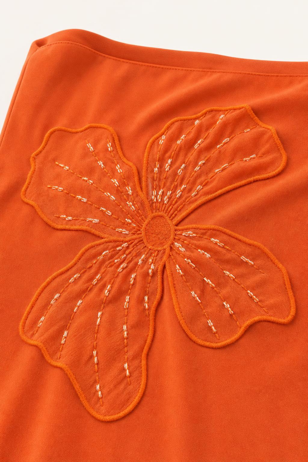Close-up of orange fabric with floral embroidery and bead accents