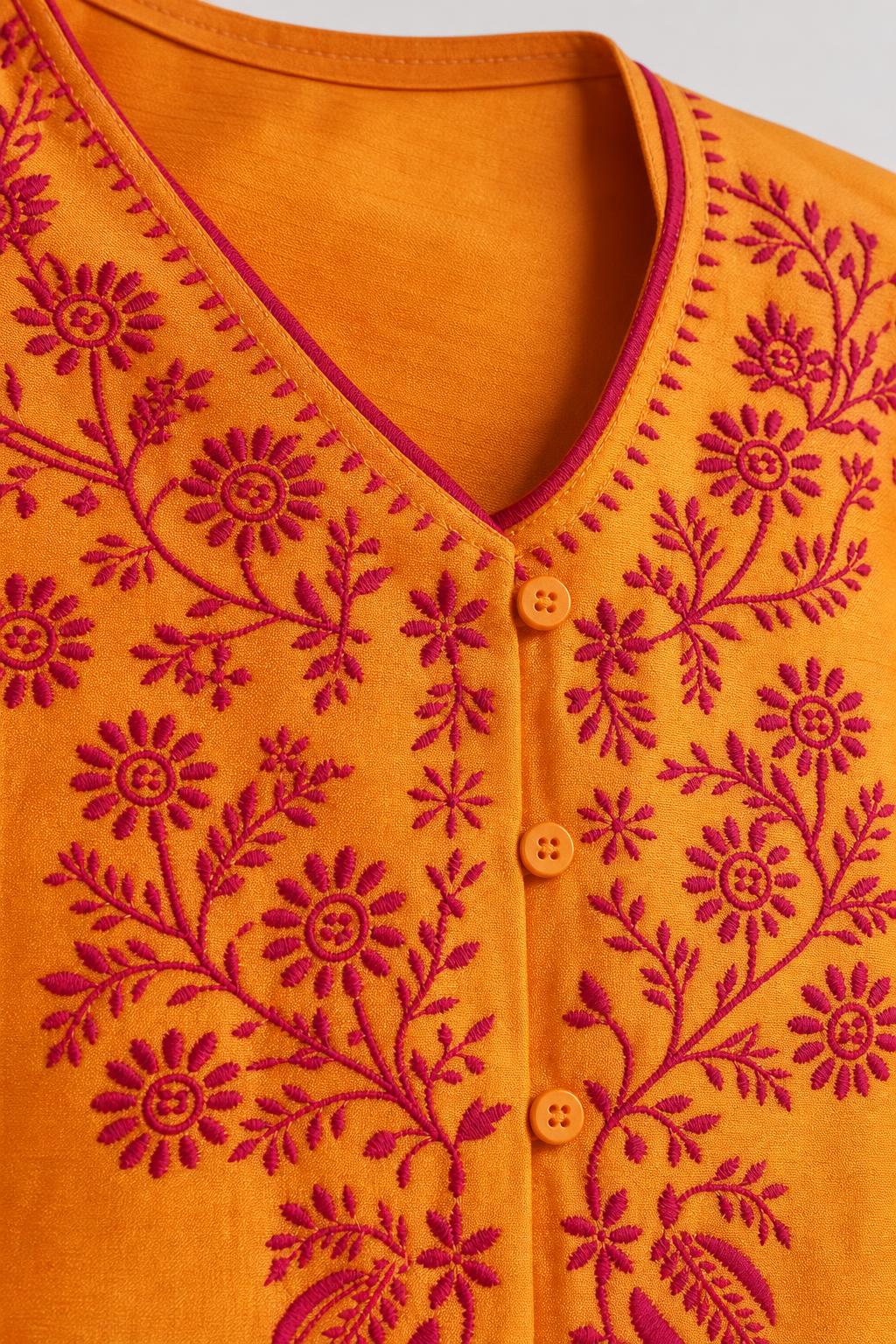 Close-up detail of V-neckline and red floral embroidery on yellow fabric