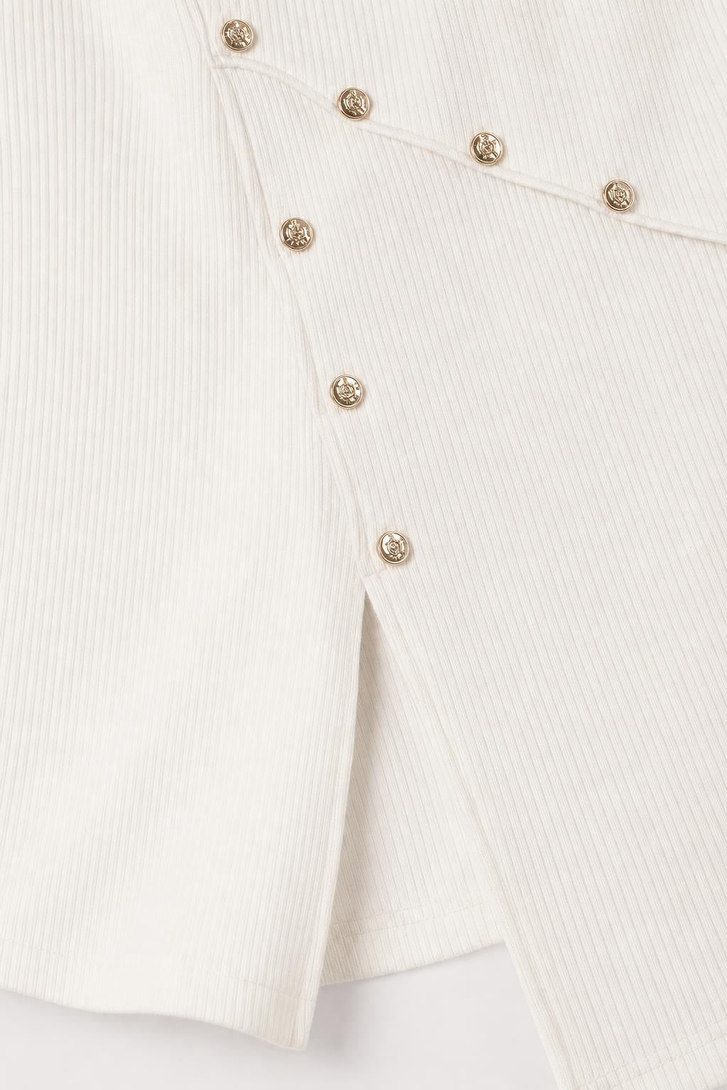 Close-up detail of gold-tone buttons and side hem slit on white dress