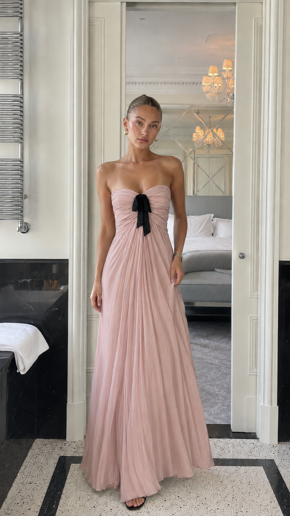 Front view of blush pink strapless pleated maxi gown with black bow detail