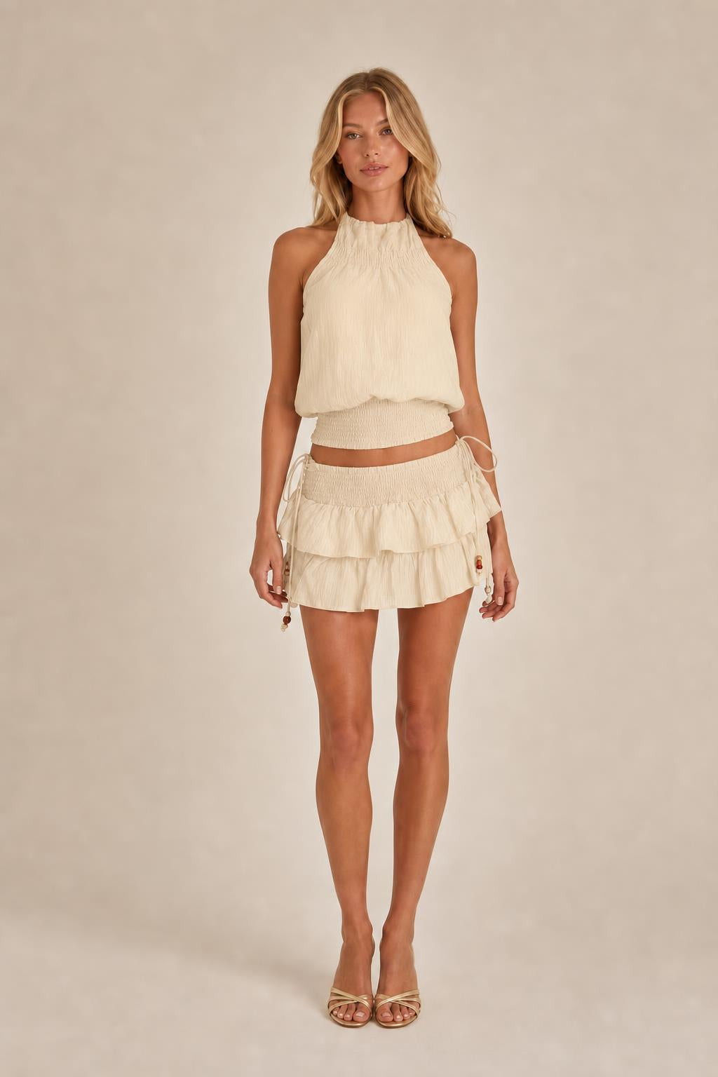 Model wearing beige halter top and ruffled mini skirt set