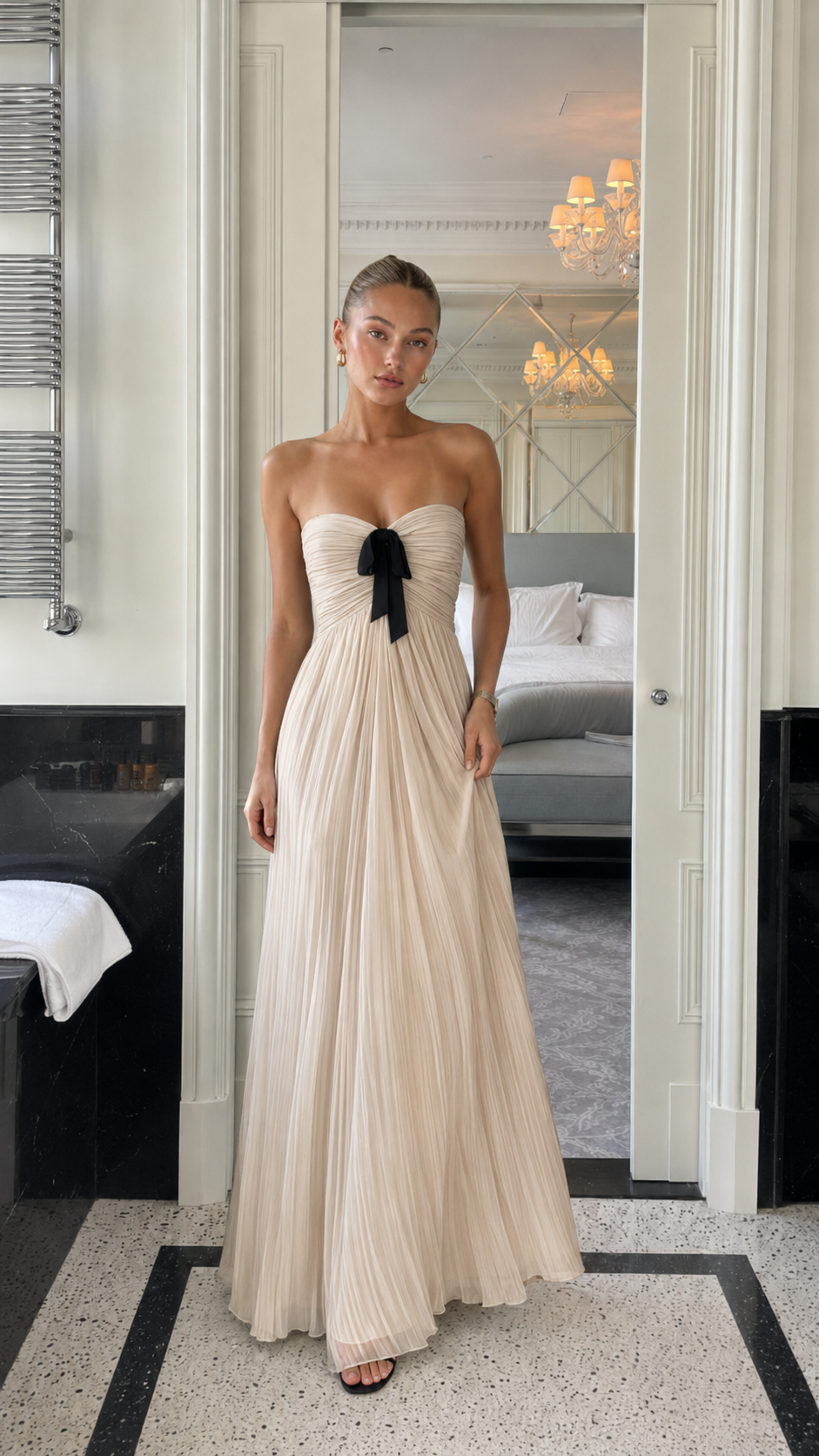 Front view of champagne strapless pleated maxi gown with black bow detail